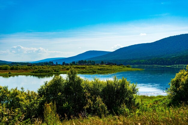 Landschaft am Flussufer in Sibirien helle, saftige Farben, hügelige Flussufer und blaue Wolken