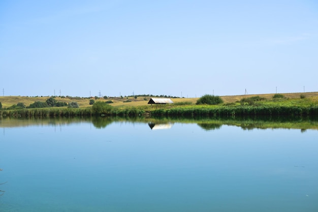 Landschaft an einem sonnigen Tag eines Sees, der durch ein grünes Feld mit einem Haus mit blauem Himmel geteilt wird