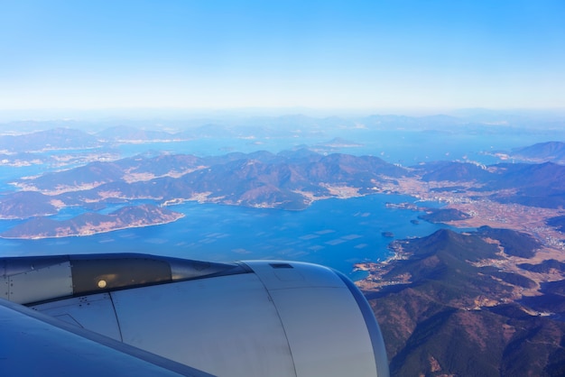 Landschaft aus dem Flugzeugfenster mit Blick auf den blauen Himmel, die südkoreanische Halbinsel, die angrenzenden Inseln und die Metropole Busan am Morgen, Südkorea