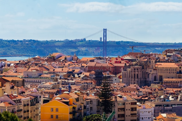 Landschaft der roten Dächer und der entfernten Brücke über Fluss in Lissabon während eines sonnigen Tages