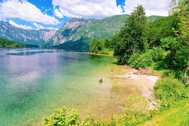 Landschaft des Bohinjer Sees in Slowenien. Menschenfischen und Natur in Slovenija. Blick auf grünen Wald und blaues Wasser. Schöne Landschaft im Sommer. Alpines Reiseziel. Berge der Julischen Alpen