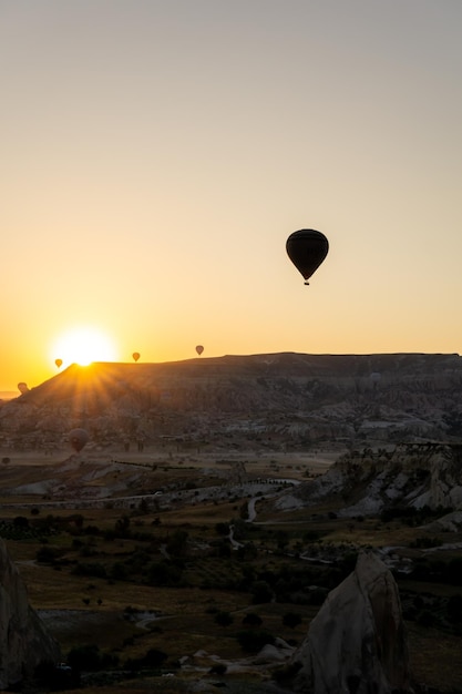 Landschaft des Love Valley in Kappadokien mit der Silhouette von Heißluftballons, die im Morgengrauen fliegen