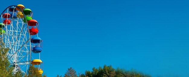 Landschaft eines Vergnügungsparks mit der Spitze eines Riesenrads, das über den Baumwipfeln gegen einen blauen Himmel zeigt