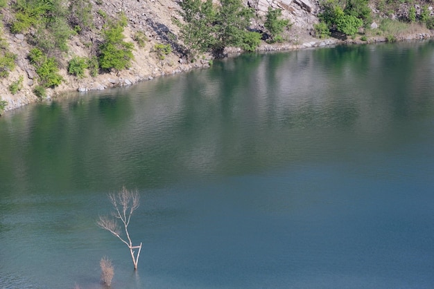 Landschaft eines verlassenen Granitsteinbruchs im Sommer mit Ästen, die aus dem Wasser ragen