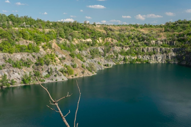 Landschaft eines verlassenen Granitsteinbruchs im Sommer mit Ästen, die aus dem Wasser ragen