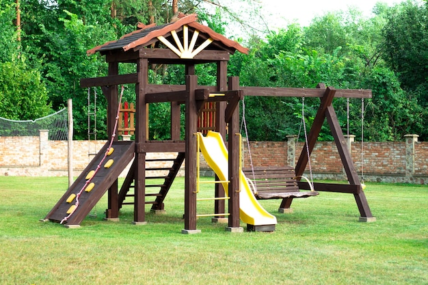 Landschaft. Holzspielplatz mit Schaukeln, Rutsche und Treppen auf dem Hintergrund eines Ziegelzauns im Innenhof des Privathauses.