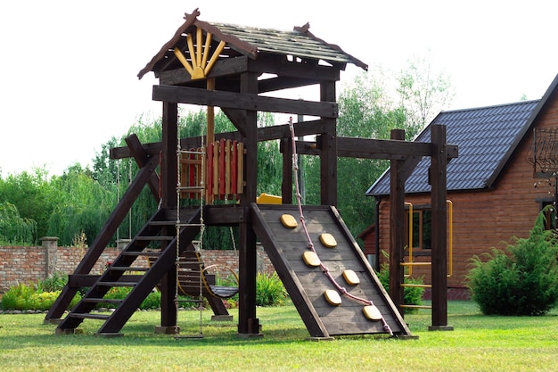 Landschaft. Holzspielplatz mit Schaukeln, Rutsche und Treppen auf dem Hintergrund eines Ziegelzauns im Innenhof des Privathauses.