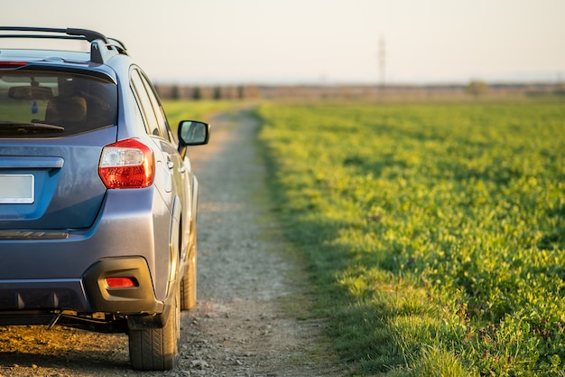 Landschaft mit blauem Geländewagen auf Schotterstraße. Reisen mit dem Auto, Abenteuer in der Tierwelt, Expedition oder extreme Reisen mit einem SUV-Auto. Offroad 4x4 Fahrzeug im Feld bei Sonnenaufgang.