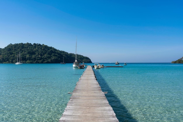 Landschaft mit Holzsteg im tropischen Meer und Sightseeing-Boot, das an sonnigen Tagen im Sommer auf Koh Kood verankert ist