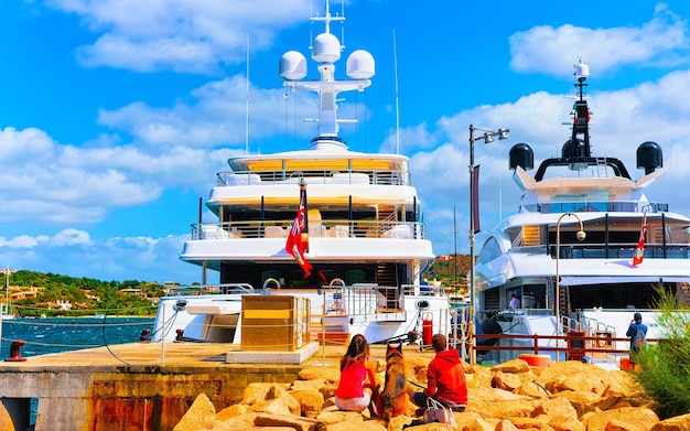 Landschaft mit Marina und Luxusyachten am Mittelmeer von Porto Cervo auf der italienischen Insel Sardinien im Sommer. Querformat auf den sardischen Stadthafen mit Schiffen und Booten in Sardinien. Gemischte Medien.