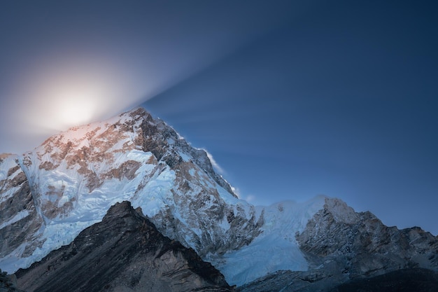 Landschaft mit Sonnenaufgang hinter schneebedeckten Bergen mit Sonnenstrahlen und Schatten über dem Himmel Nepal Himalaya