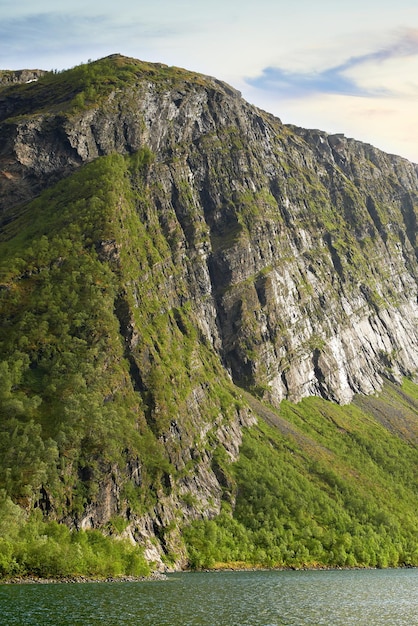 Landschaft von Bergweiden im Hintergrund eines Sees in Norwegen Üppiger Hügel mit Weide in der Nähe von Wasser im Freien Detailansicht eines Hügels hinter einem ruhigen Fluss in der Natur mit Wolken am Himmel