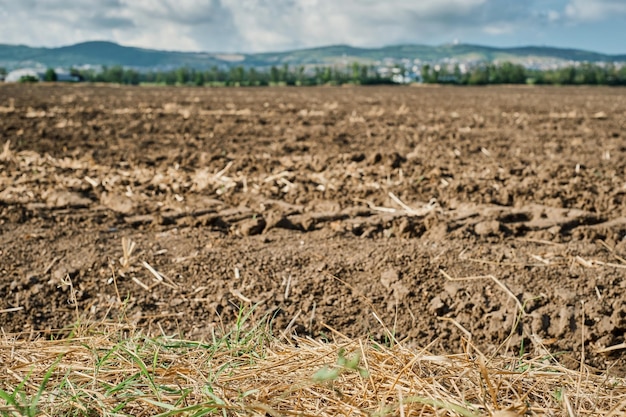 Landschaft von gepflügtem Land auf einem Bauernhof mit blauem Himmel mit Wolken Selektiver Fokus auf Stroh im Vordergrund unscharfer Hintergrund Panorama von ruhendem Land nach der Sommerernte von landwirtschaftlichen Kulturen