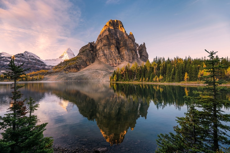 Foto landschaft von sunburst see und von berg assiniboine-reflexionen zwischen kiefer bei sonnenaufgang