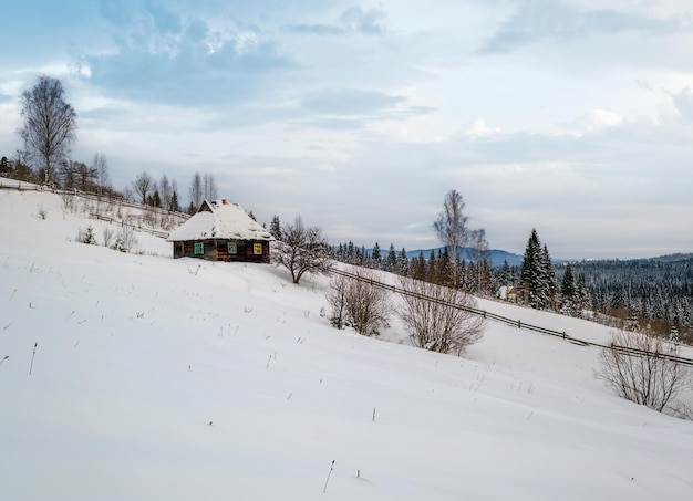 Landschaftliche Hügel, Gärten und Ackerland im Winter, abgelegenes alpines Bergdorf und ein kleines altes verlassenes Haus am Hügel.