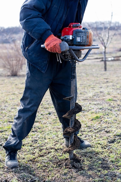 Landwirt, der handgehaltene Bodenbohrmaschinen oder tragbare manuelle Erdbohrer verwendet, um den Boden für das Pflanzen von Bäumen vorzubereiten