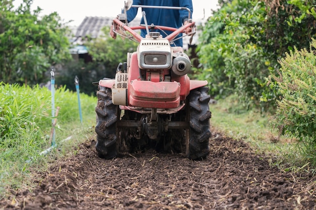 Landwirt, der Zweiradschlepper kontrolliert, der auf Bodenfeld in Plantage pflügt