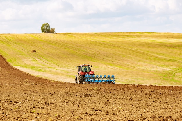 Landwirt im roten Traktor, der Land mit Pflug für die Aussaat vorbereitet
