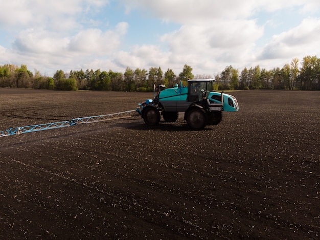 Landwirtschaftliche Frühlingsarbeit auf den Feldern. Der Traktor besprüht Pflanzen mit Herbiziden, Insektiziden und Pestiziden.