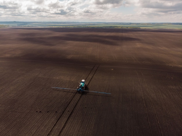 Landwirtschaftliche Frühlingsarbeit auf den Feldern. Der Traktor besprüht Pflanzen mit Herbiziden, Insektiziden und Pestiziden.