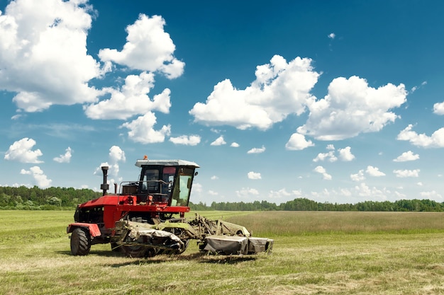 Landwirtschaftliche Maschinerie, Erntemaschine, die Gras auf einem Gebiet gegen einen blauen Himmel mäht