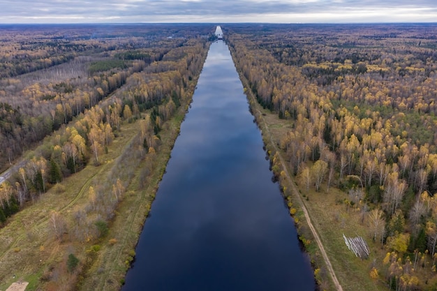 Langer gerader Kanal, der sich durch Wald erstreckt, mit Wolken, die sich in stillem Wasser widerspiegeln Russland