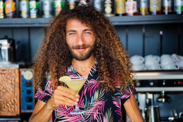 Langer, lockiger Mischlingsbarmann, der in der Strandhütte in Tropen ein alkoholisches Getränk zubereitet