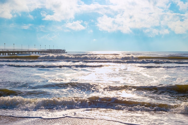 Langer Pier im blauen Meer mit Welle und Himmel mit Wolken