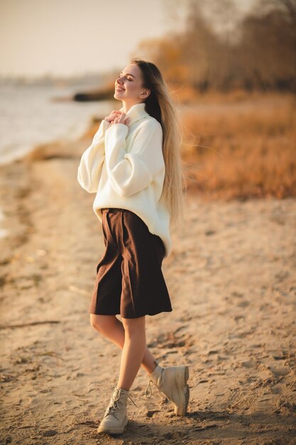 Langhaariges blondes Mädchen, das am Herbstmorgen am Sandstrand sitzt