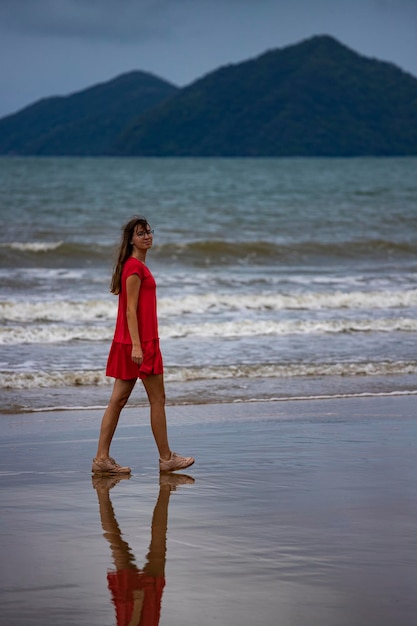 Langhaariges Mädchen im roten Kleid geht am tropischen australischen Strand mit Inseln im Hintergrund entlang