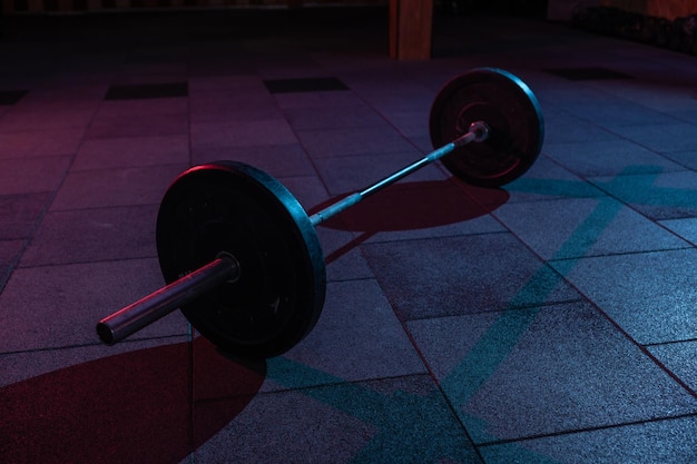 Langhantel in einem dunklen grungigen Fitnessstudio mit blau-rotem Neonlicht