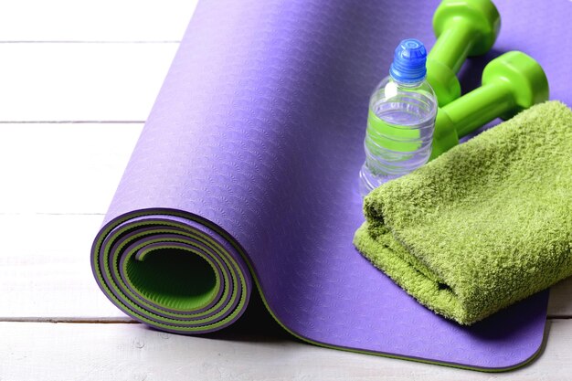 Langhanteln in der Nähe von Wasserflasche und weichem Handtuch auf Yogamatte