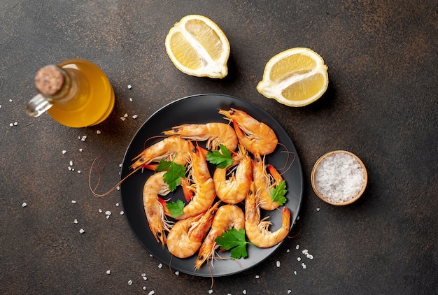 Langostinos crudos en un plato negro con hierbas y especias sobre un fondo de piedra