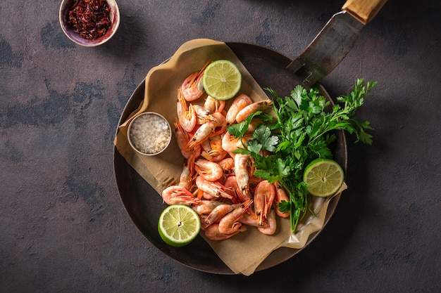 Langostinos crudos en una sartén con ingredientes para cocinar en una vista superior oscura