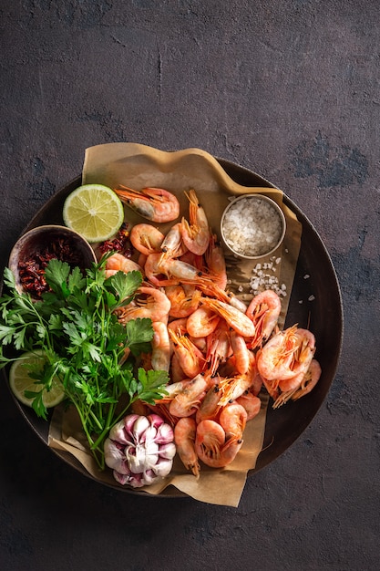 Langostinos crudos en una sartén con ingredientes para cocinar en una vista superior oscura