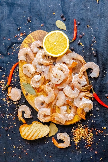 langostinos de gambas rojas enteras peladas, limón, sal marina grande, sobre una pizarra oscura con verduras