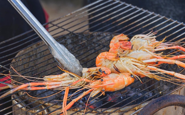 Langostinos a la parrilla con pinzas de acero en parrilla de carbón en el área al aire libre