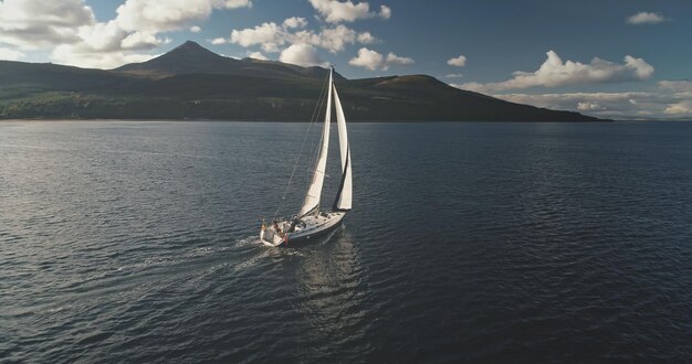 Langsam bewegte Yacht segelt an der Küste einer Berginsel Luft Weißes Segelboot bei Arran Schottland Europa