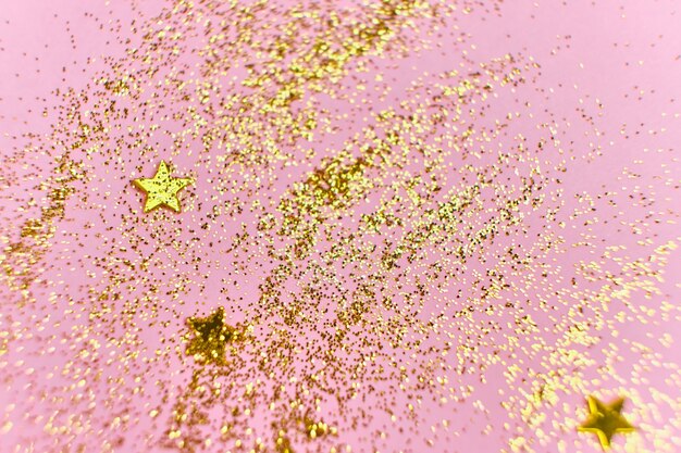 Lantejoulas com glitter dourado e estrelas em uma superfície rosa