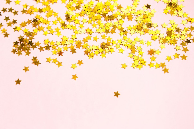 Lantejoulas douradas em forma de estrelas cintilam sobre um fundo rosa. Planos de fundo com copyspace para um feriado, decoração de festa, Natal e ano novo, aniversário e aniversário. Gradiente e textura