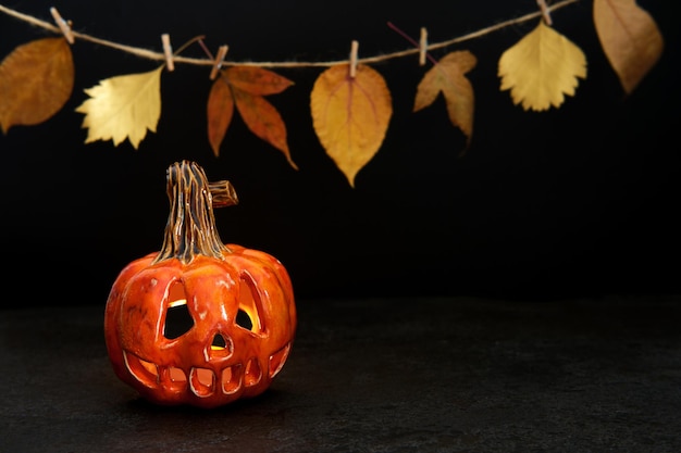 Lanterna de abóbora cerâmica de Halloween e guirlanda de folhas de outono em fundo preto Cartão de saudação