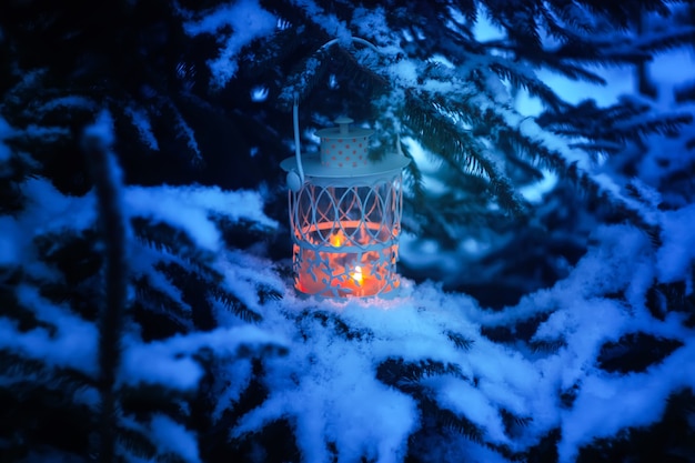 Lanterna de Natal decorativa com vela acesa pendurada no galho de árvore do abeto coberto de neve em um parque de inverno. Cartão festivo de ano novo, cartaz, design de cartão postal.