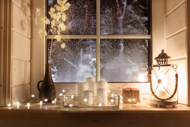 Lanterna de natal festiva, presentes e velas no parapeito de uma janela de madeira no inverno dentro de casa. decoração de natal, estilo escandinavo