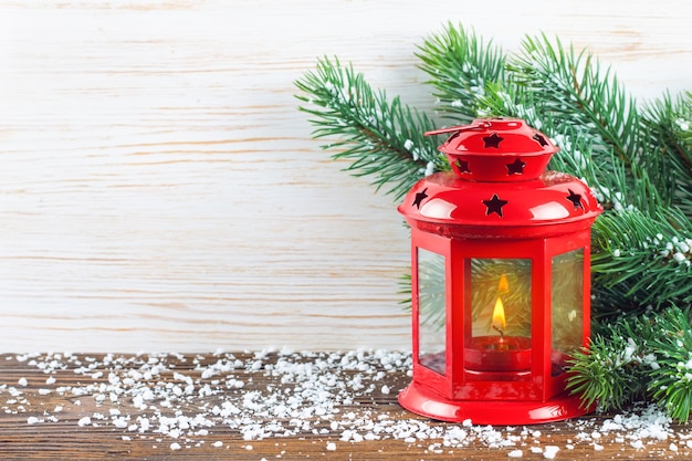 Lanterna vermelha com uma vela acesa e decoração de ano novo sobre neve e fundo branco de madeira