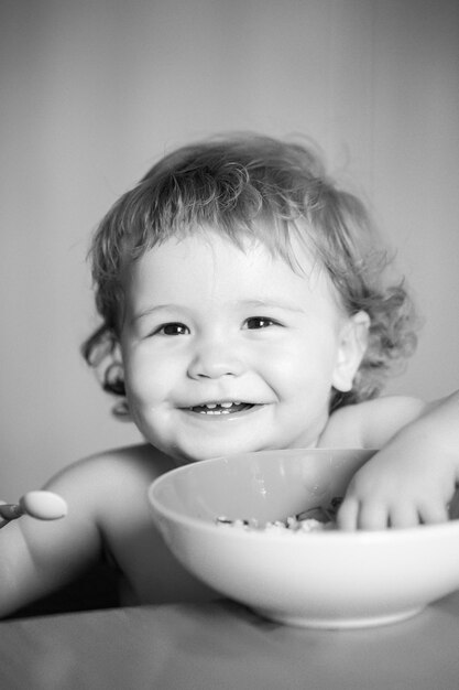 Lanzamiento niño comer niño bebé comer sopa en la cocina con platos y cuchara cara de niño divertido primer plano