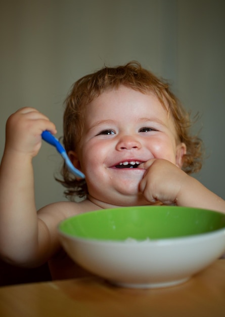 Lanzamiento de niño comiendo comida Gracioso bebé comiendo comida él mismo con una cuchara en la cocina