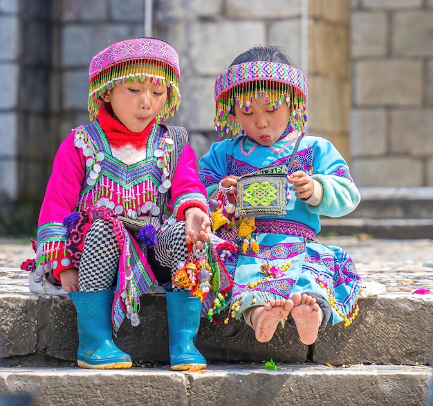 Lao Cai VIETNAM 12 de março de 2023 belo retrato de uma garotinha vietnamita HMong minoria étnica cumprimenta turistas sentados em frente à igreja e vende itens artesanais no centro de Sapa