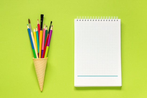 Lápices coloreados en el cono de helado, cuaderno en fondo verde. Concepto de regreso a la escuela