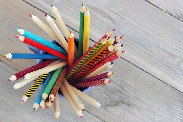 Lápices coloreados en una taza en la tabla de madera, visión superior.