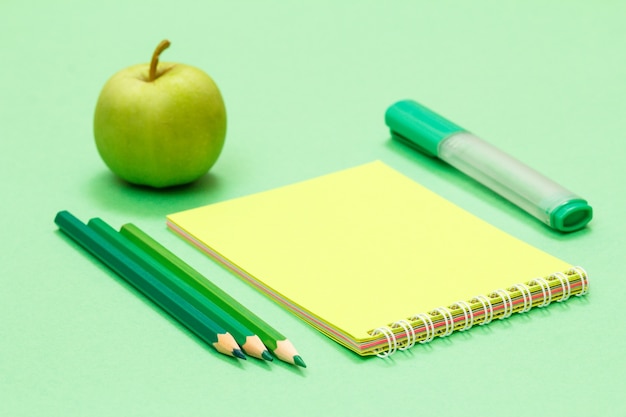 Lápices de colores, cuaderno, rotulador y manzana sobre fondo verde. Concepto de regreso a la escuela. Suministros escolares. Poca profundidad de campo.